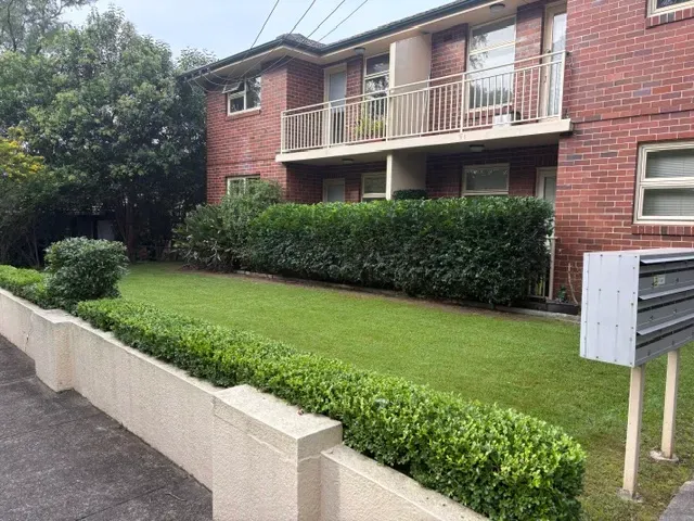 Lawn and low hedge maintained along the front of a brick unit block